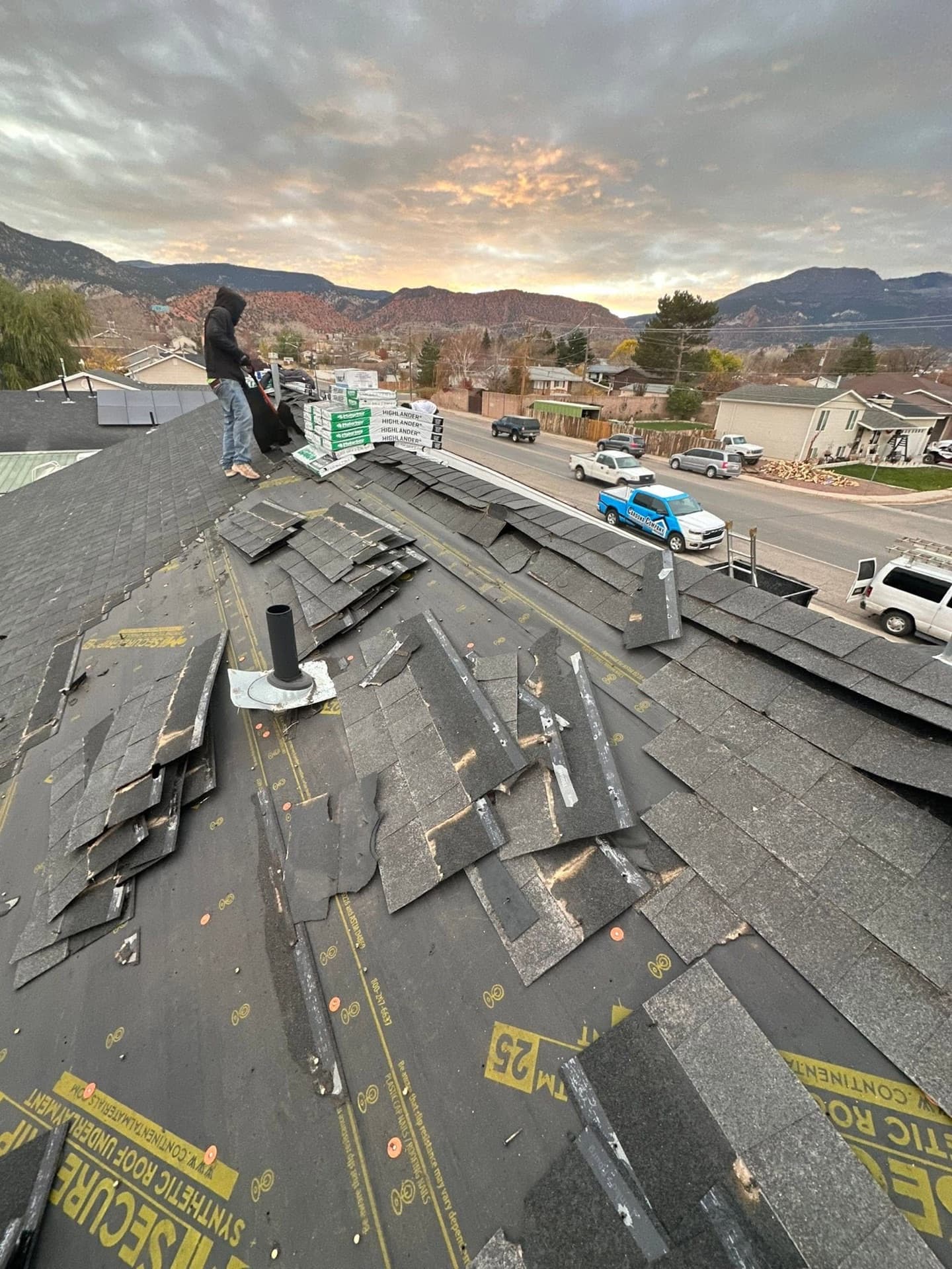 Cardona Company crew tearing off an old roof at sunset with Southern Utah's red-rock cliffs in the background