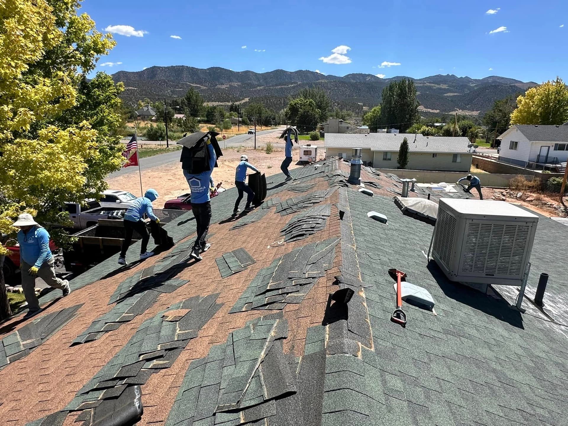 Cardona Company roofing crew removing old shingles on a Southern Utah home with mountains in the distance