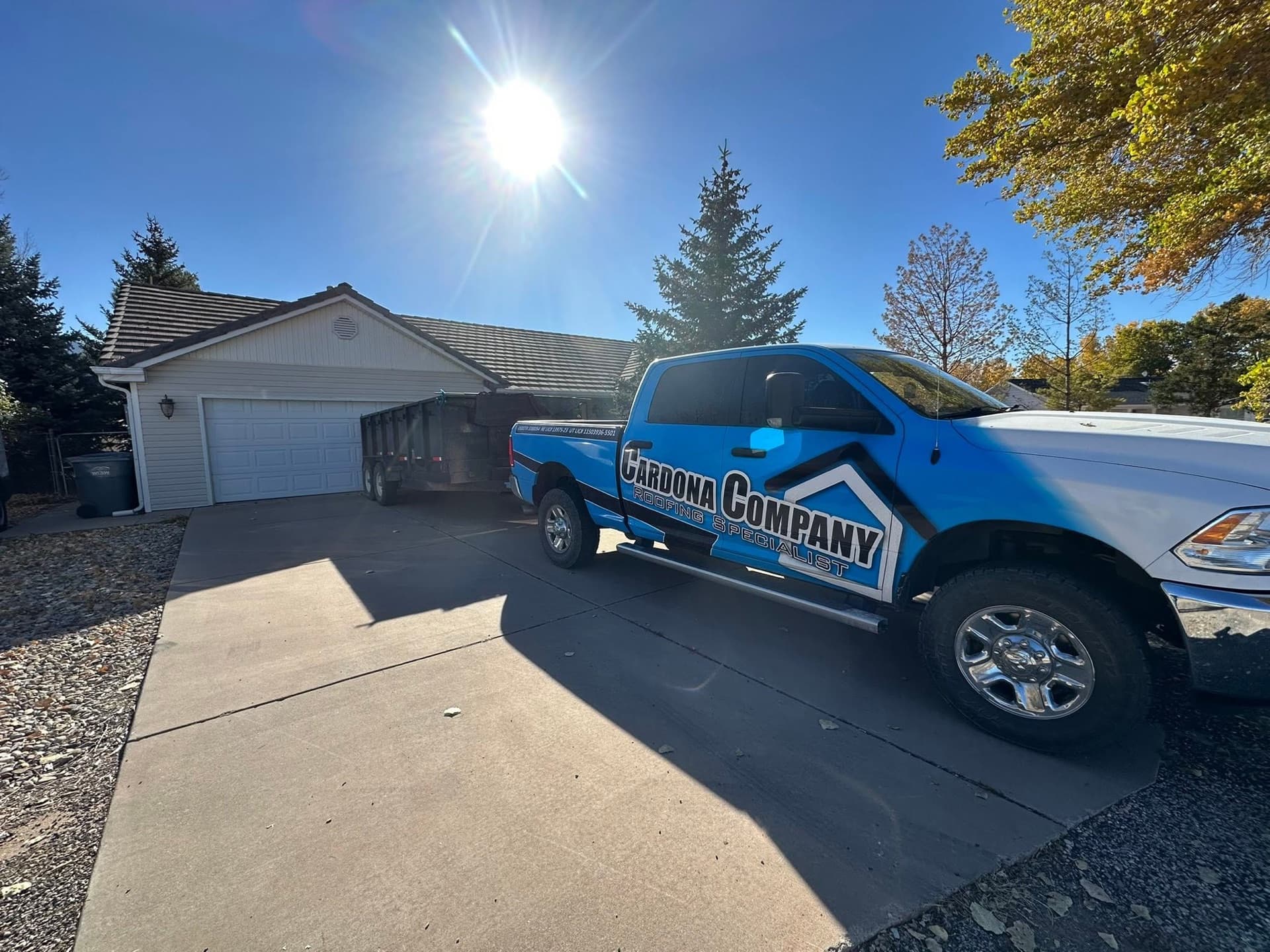 Cardona Company truck and dump trailer on a completed roofing job on a sunny Utah day