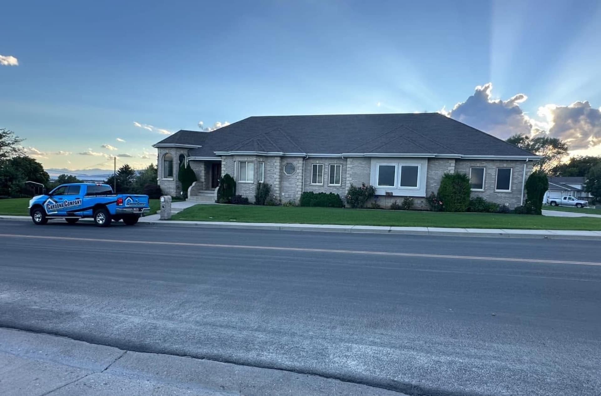 Completed roof on a brick Cedar City home at dusk with the branded Cardona Company truck out front