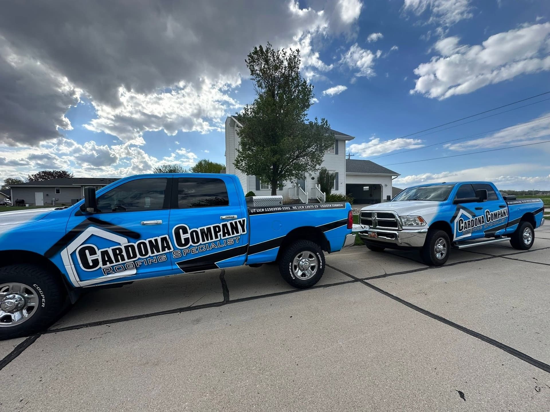 Two branded Cardona Company trucks parked at a completed roofing project
